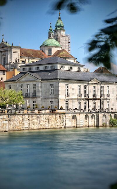 Historic stone building and St. Ursus Cathedral bordering the Aare River in Solothurn, Switzerland. Unsplash@Martin Zenker