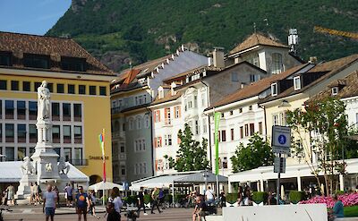 People walking and cycling through a sunny square in Bolzano, Italy. Unsplash@Babak Habibi