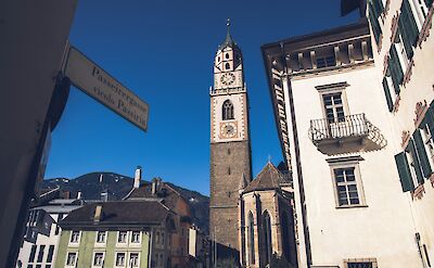 Stone clock tower of the St. Nikolaus Church in Merano, Italy. Unsplash@Alessio Zaccaria