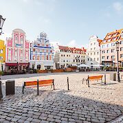 Berlin to Malchin - A cobblestone square with colorful, historic buildings in a European town, featuring benches and street lamps.