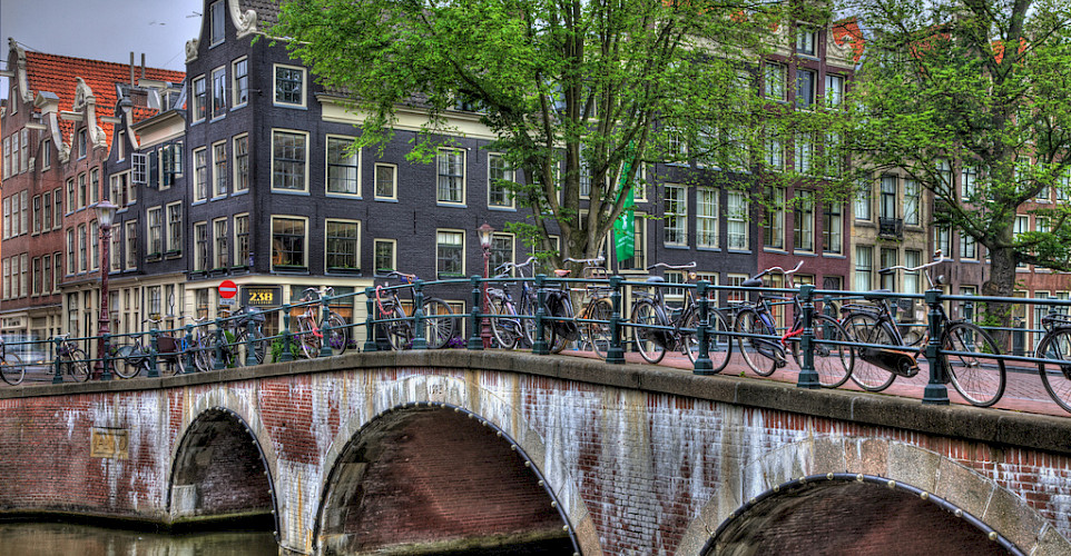Bikes over the canal bridge in Amsterdam, North Holland, the Netherlands. Photo via Flickr:vgm8383 52.370352, 4.88456