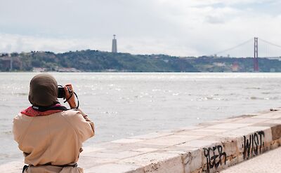 Taking a photo of the red bridge over the River Tagus, Lisbon, Portugal. Unsplash: Suad Kamardeen