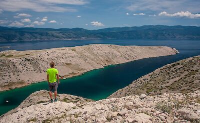 Hiker overlooking a deep turquoise bay. toST