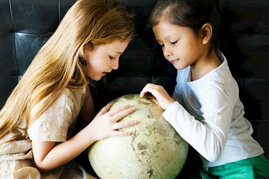 Two girls looking at a globe to choose their next family bike tour destination. Unsplash@Getty Images