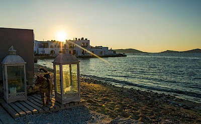 Golden-hour view of Paros with boats, calm waters, and Cycladic houses at sunset. toIH