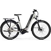 Merida silver step-through electric mountain bike with a black rear rack, front suspension, and knobby tires against a white background.