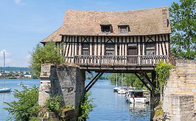 A historic timber-framed building spanning the Seine river in Les Andelys. toTN