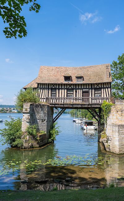 A historic timber-framed building spanning the Seine river in Les Andelys. toTN