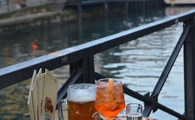 Aperitivo by the canal, with Aperol Spritz and Italian snacks. Pexels:ValeriDrozdova