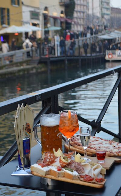 Aperitivo by the canal, with Aperol Spritz and Italian snacks. Pexels:ValeriDrozdova
