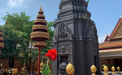 Flowers blooming around a sculpture in Siem Reap, Cambodia bike tour. Unsplash@Claire Pins Travel