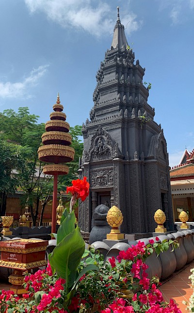 Flowers blooming around a sculpture in Siem Reap, Cambodia bike tour. Unsplash@Claire Pins Travel
