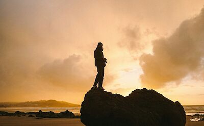 Standing on a rock at sunset in San Vicente de la Barquera, Spain. Unsplash:Paulina Herpel