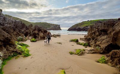 Woman walking her dog on the beach in Llanes, Spain. Unsplash:Juan Gomez