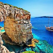 Multi-Adventure Tour in the Ionian Islands - Tourist boat passing next to Trypitos (also known as "Kamara"), a natural rocky arch at Paxos island, Ionian Sea, GREECE. In the background, Antipaxos island.