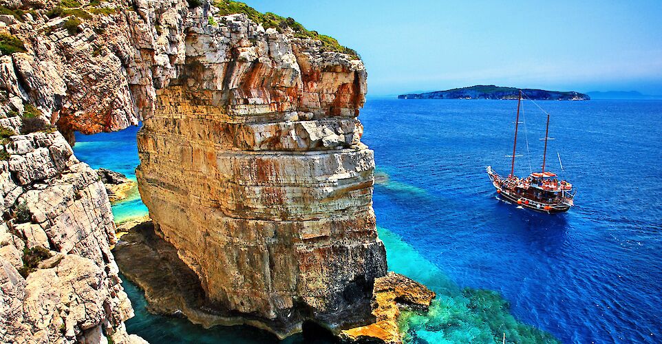 Tourist boat passing next to Trypitos (also known as "Kamara"), a natural rocky arch at Paxos island, Ionian Sea, GREECE. In the background, Antipaxos island.