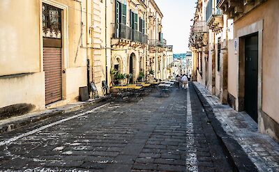 Sunlit street lined with honey-colored Baroque palaces in Noto. Flickr:MichaelGaylard